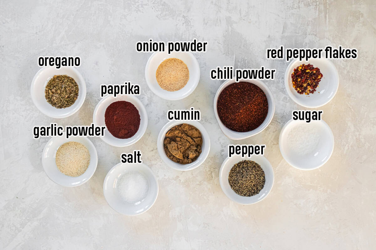Ingredients for low sodium taco seasoning including chili powder, cumin, paprika, garlic powder, onion powder, oregano, salt, black pepper, sugar, and red pepper flakes in small white bowls.