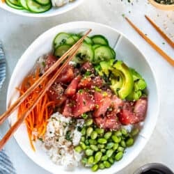 Ahi tuna poke bowl with marinated tuna, avocado, cucumber, carrot, edamame, and crab over white rice with chopsticks.