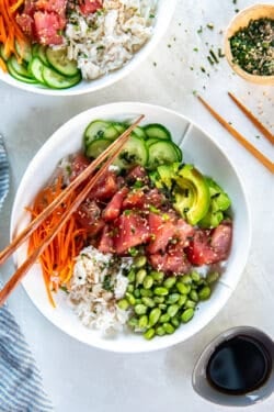 Ahi tuna poke bowl with marinated tuna, avocado, cucumber, carrot, edamame, and crab over white rice with chopsticks.