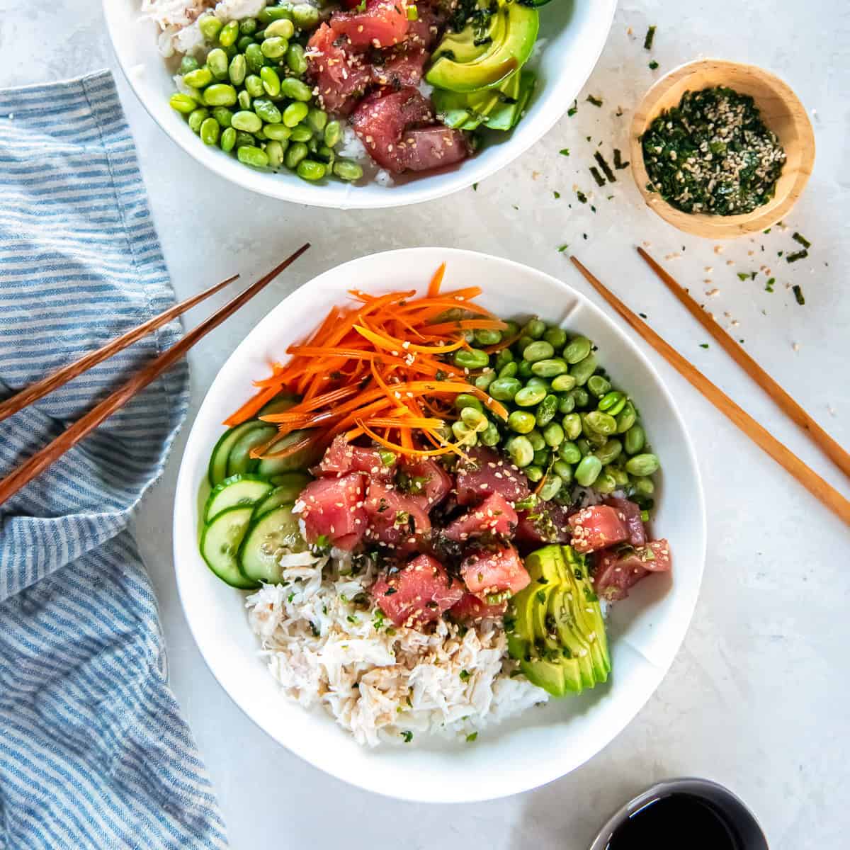 Two ahi tuna poke bowls with white rice, marinated tuna, crab meat, avocado, cucumber, carrot, and edamame arranged in sections.