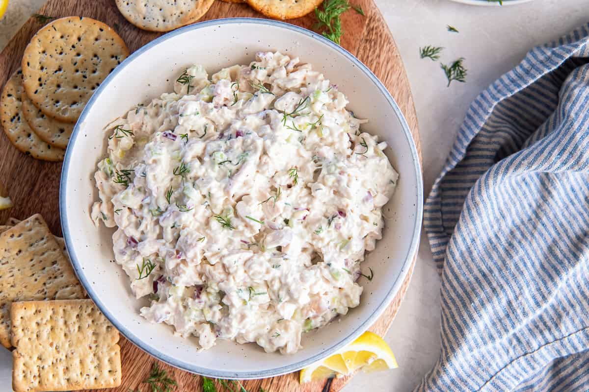 Cottage cheese chicken salad with crackers and lemon wedges on a wooden serving board.