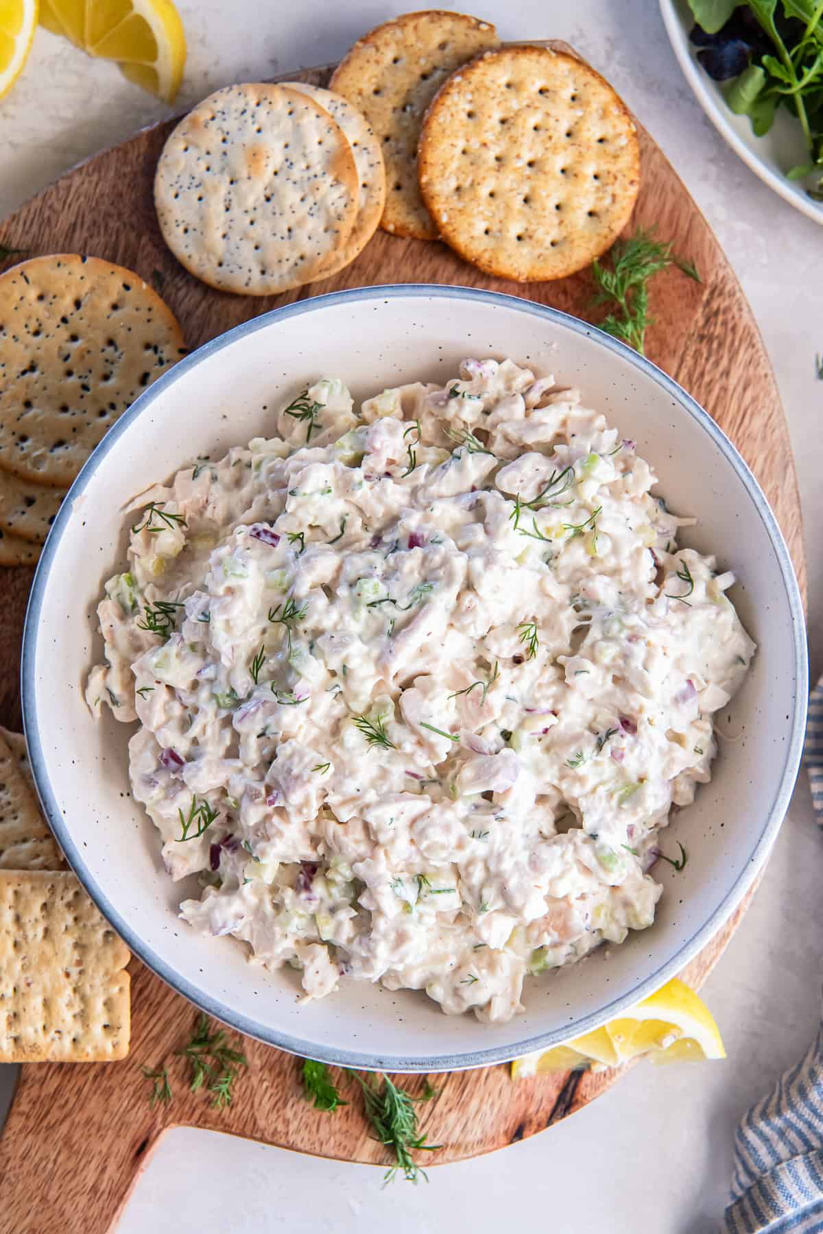 A bowl of cottage cheese chicken salad in a bowl with crackers, lemon wedges, and fresh dill.