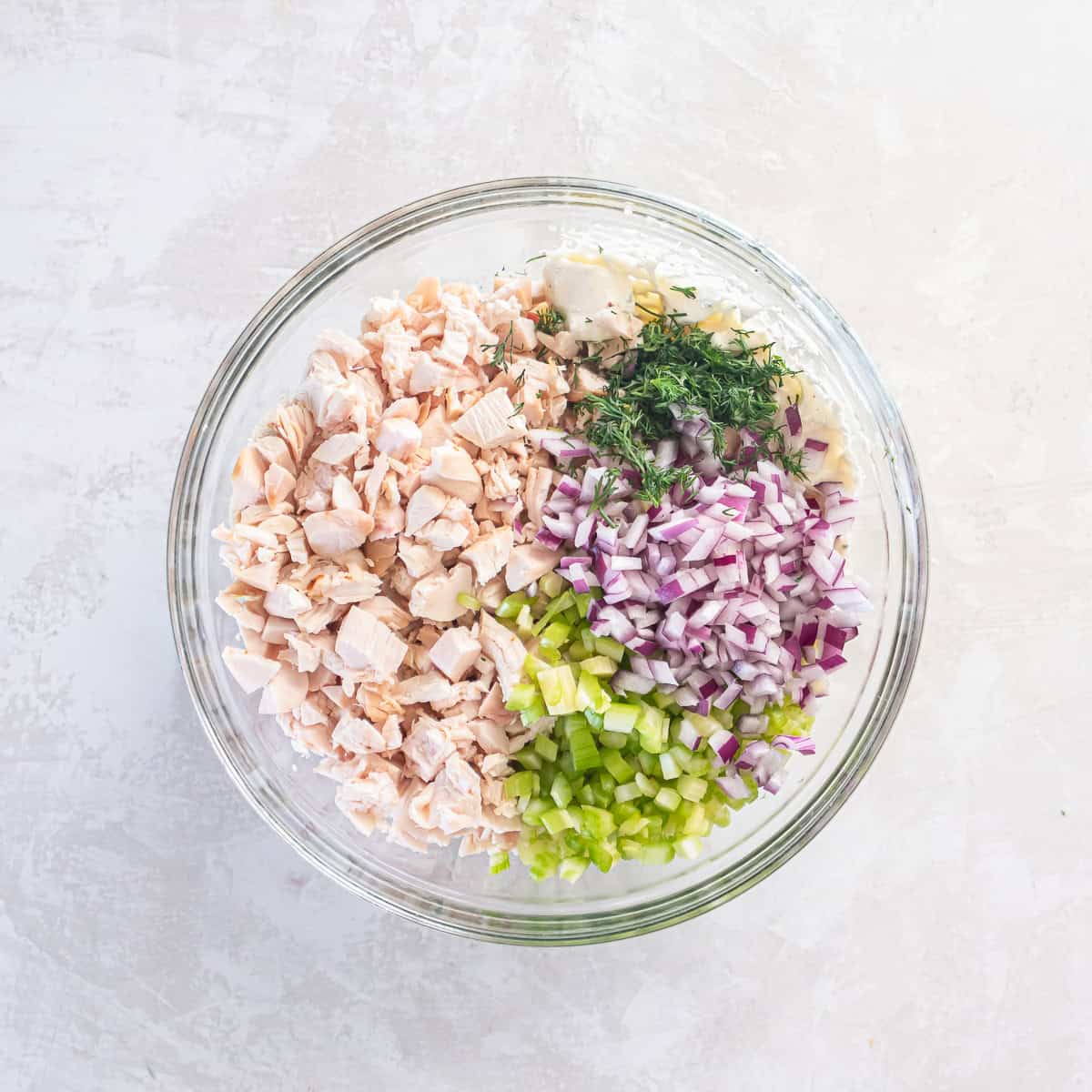 Chicken, red onion, celery, and dill on top of blended cottage cheese in a bowl.