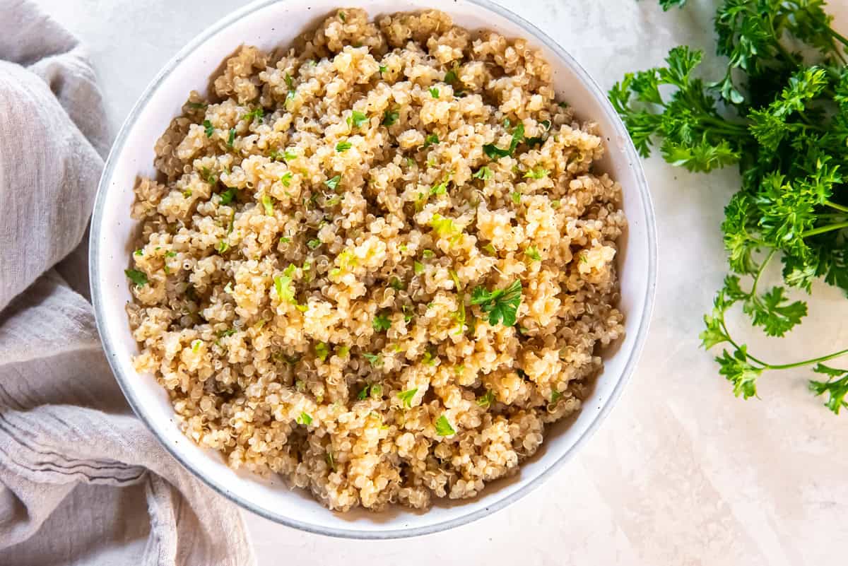 Garlic butter quinoa in a white bowl garnished with chopped parsley on a light surface with a linen napkin.