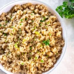 Garlic butter quinoa cooked in broth and garnished with fresh parsley in a white bowl.