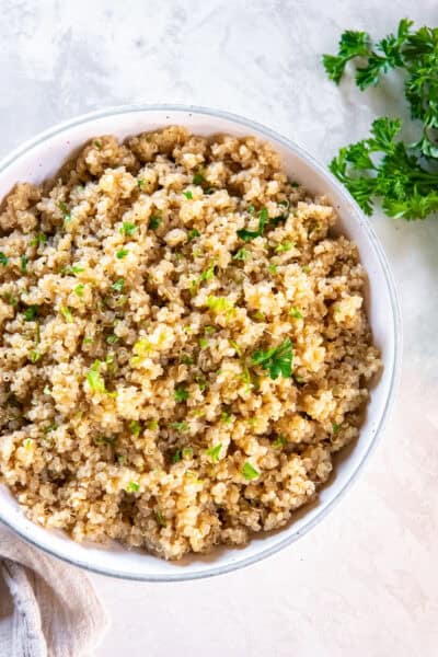 Garlic butter quinoa cooked in broth and garnished with fresh parsley in a white bowl.