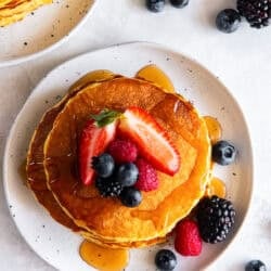 Cottage cheese pancakes topped with strawberries, blueberries, raspberries, and maple syrup on a plate.