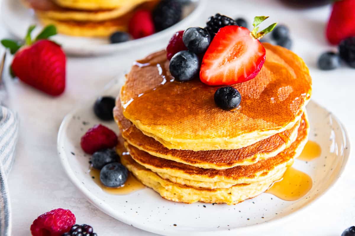 Stack of cottage cheese pancakes topped with strawberries, blueberries, and blackberries with maple syrup.