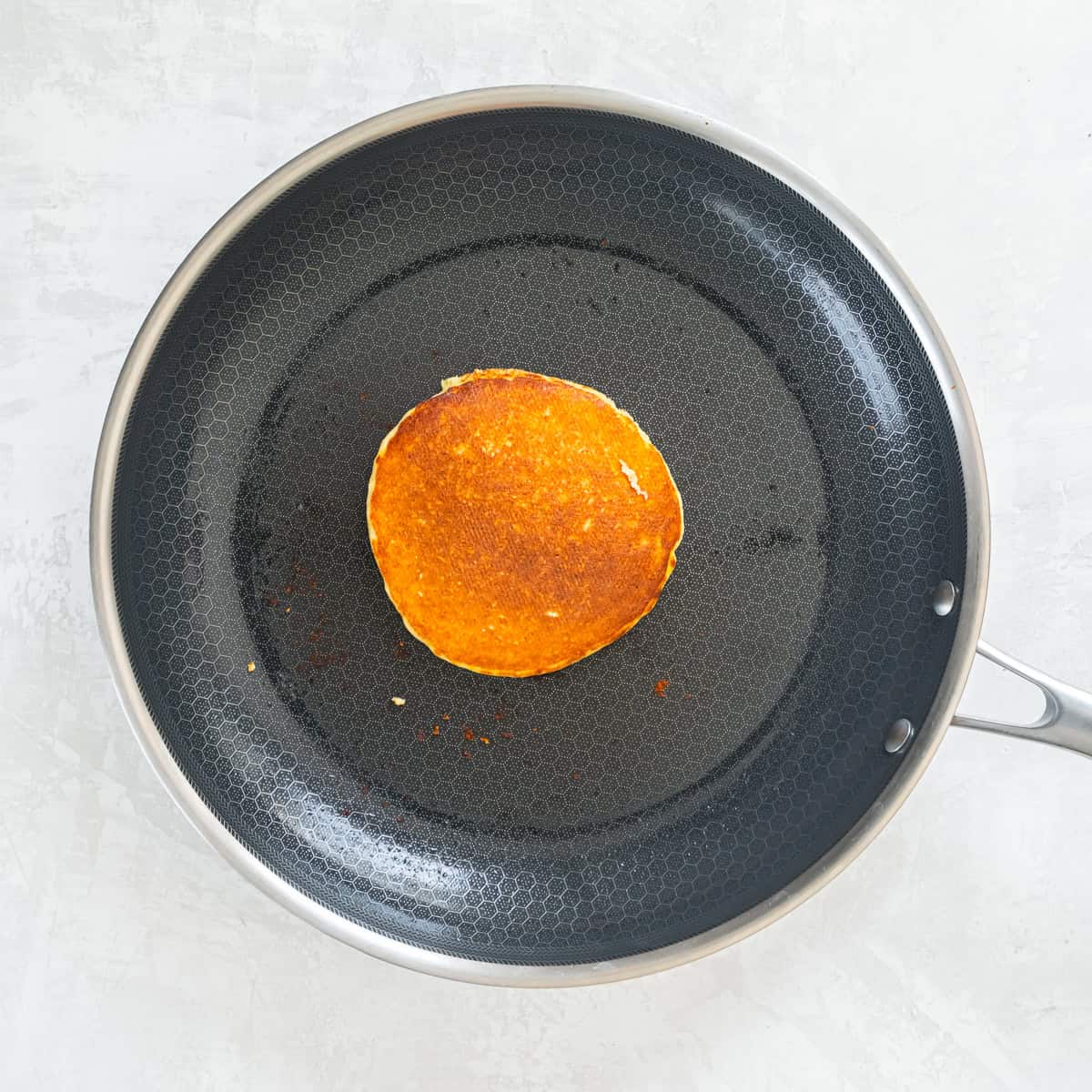 Cottage cheese pancake browned on one side cooking in a skillet.