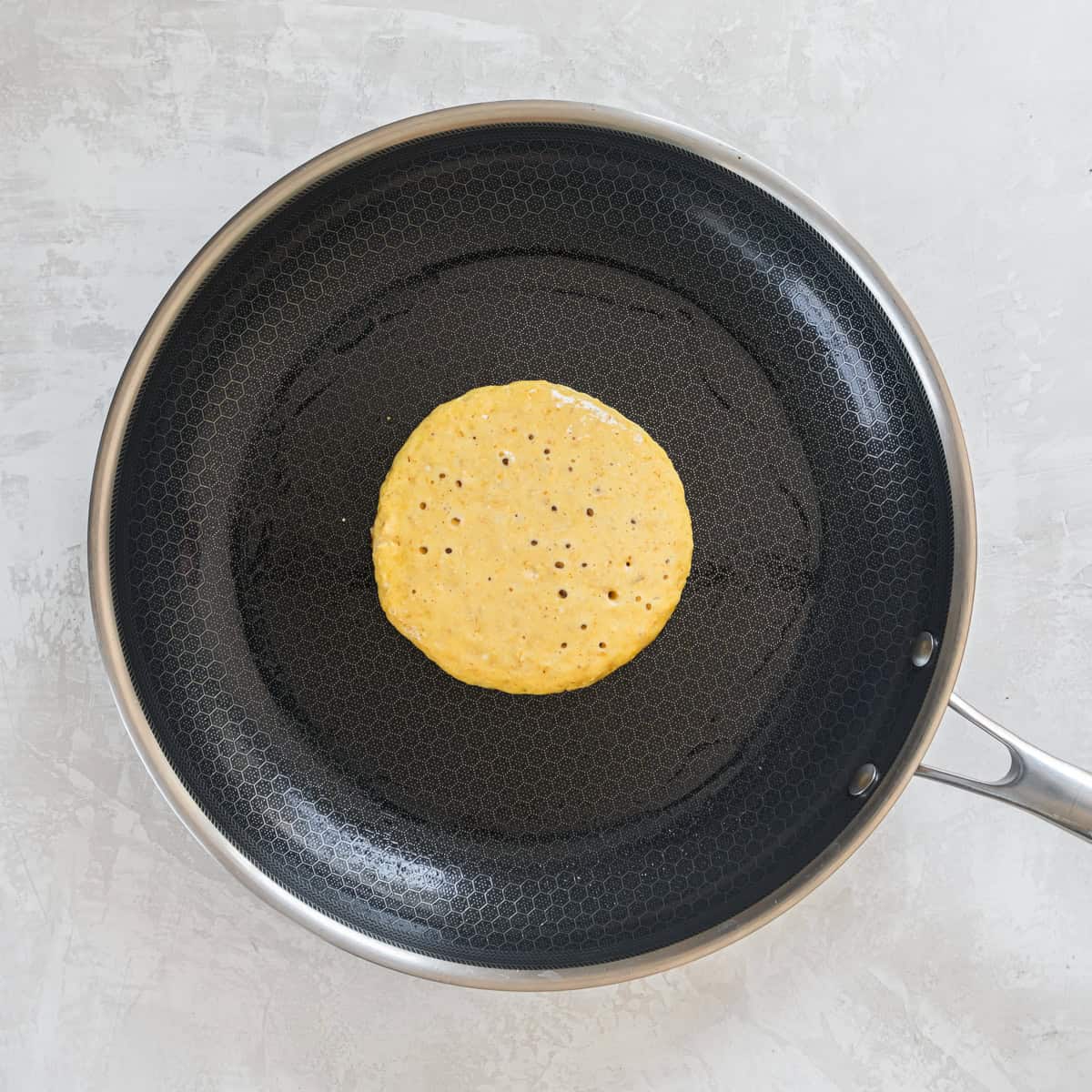 Cottage cheese pancake cooking in a nonstick skillet before flipping.