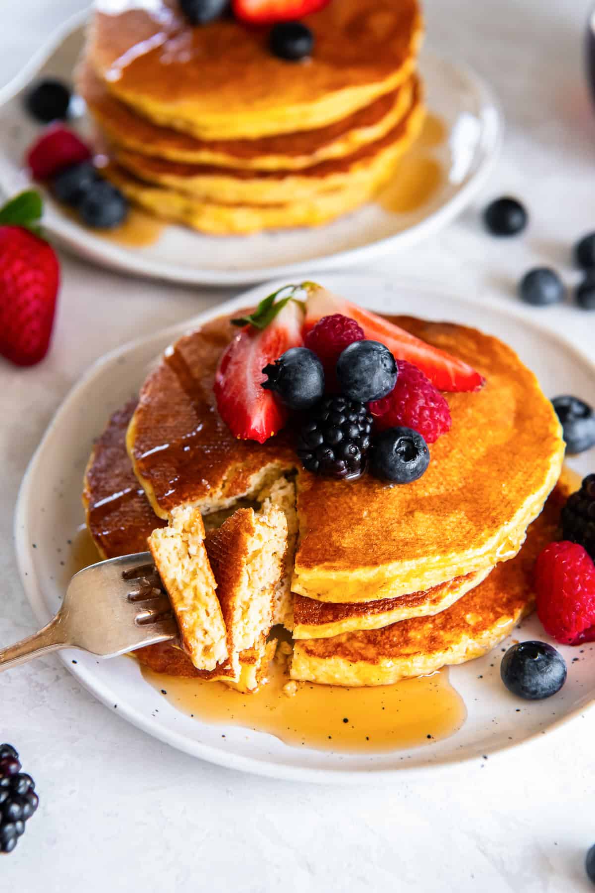 Cottage cheese pancakes topped with fresh berries and maple syrup, with a fork cutting into a fluffy stack.