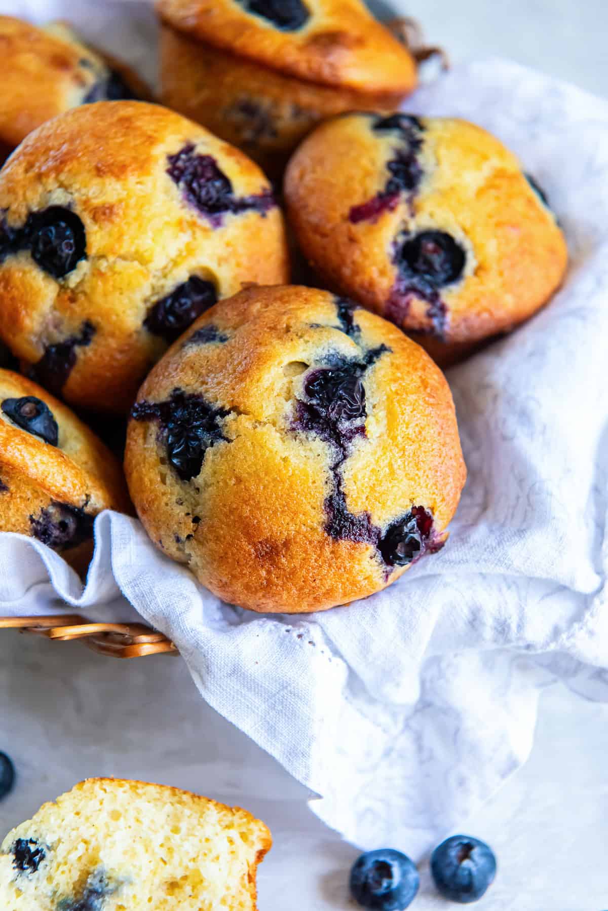 Golden brown non-dairy blueberry muffins made with silken tofu, arranged in a basket lined with a cloth.