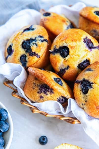 Blueberry muffins made with silken tofu with golden tops and juicy blueberries in a basket.