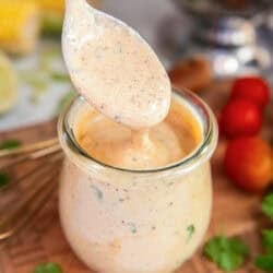 Spoon lifting creamy cilantro lime dressing above a glass jar, showing the thick, creamy texture with visible herb flecks.