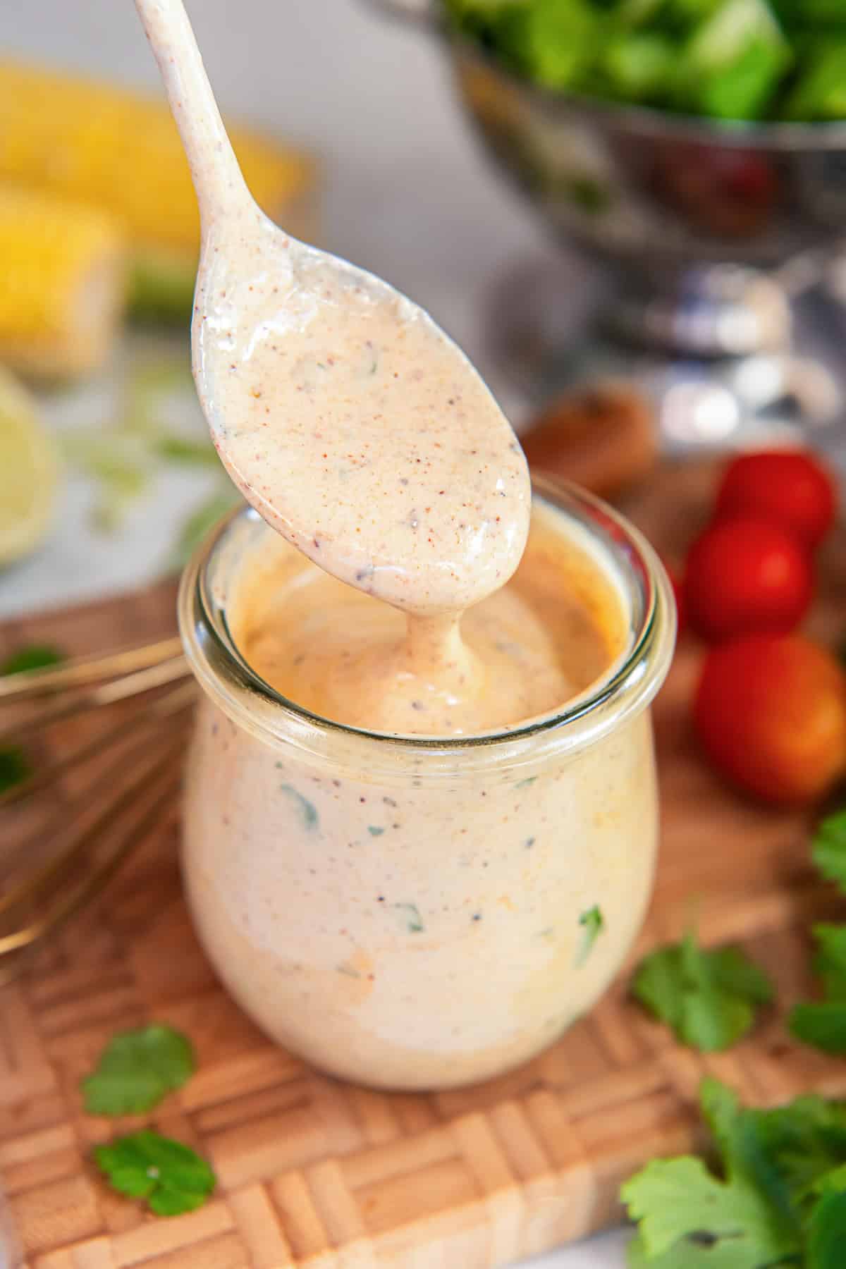Spoon lifting creamy cilantro lime dressing above a glass jar, showing the thick, creamy texture with visible herb flecks.