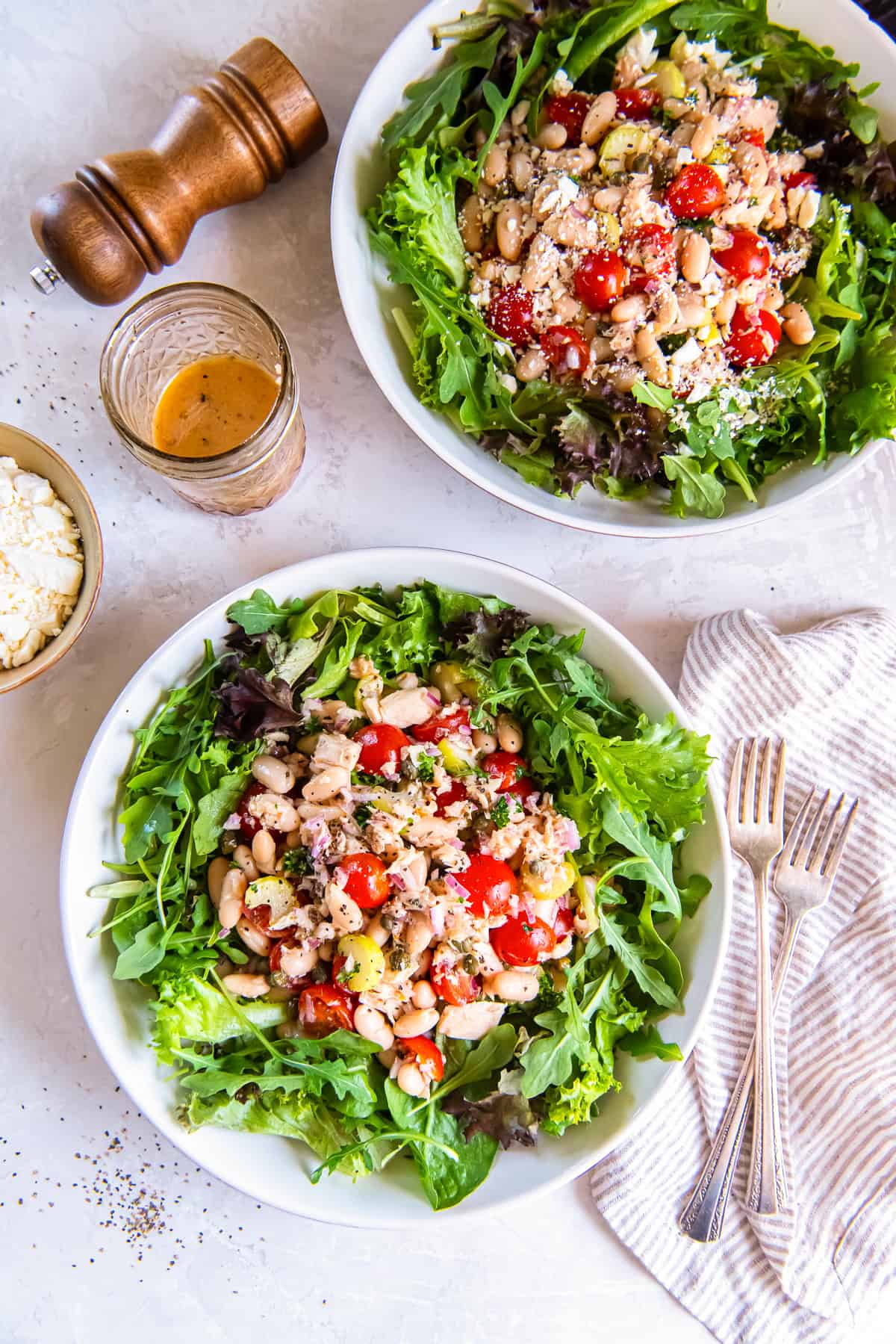 Two bowls of White Bean Tuna Salad over mixed greens with cherry tomatoes, cannellini beans, feta cheese, and a homemade vinaigrette.