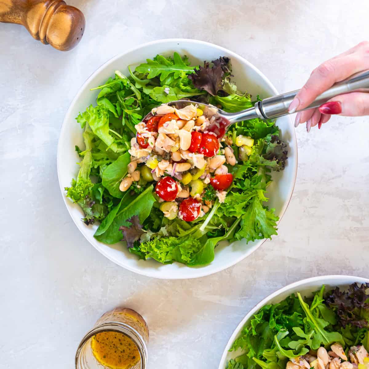 Spoonful of tuna and white bean salad with cannellini beans, cherry tomatoes, celery, and red onion being served over mixed greens in a large salad bowl.
