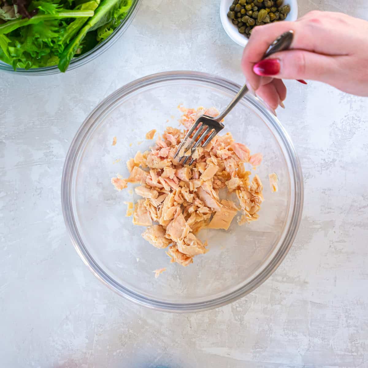 Albacore tuna being broken into chunks with a fork in a glass mixing bowl for Tuna and White Bean Salad.
