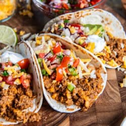 Tacos filled with ground beef taco meat and red lentils, topped with cheese, pico de gallo, avocado, lettuce, and sour cream.
