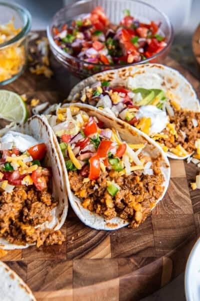 Tacos filled with ground beef taco meat and red lentils, topped with cheese, pico de gallo, avocado, lettuce, and sour cream.