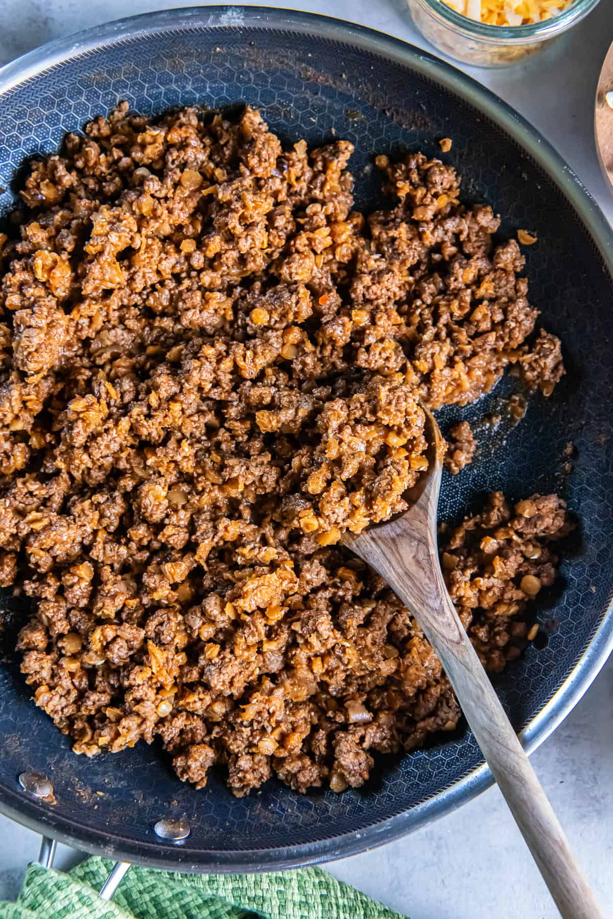 A wooden spoon scooping seasoned ground beef taco meat with red lentils from a skillet.