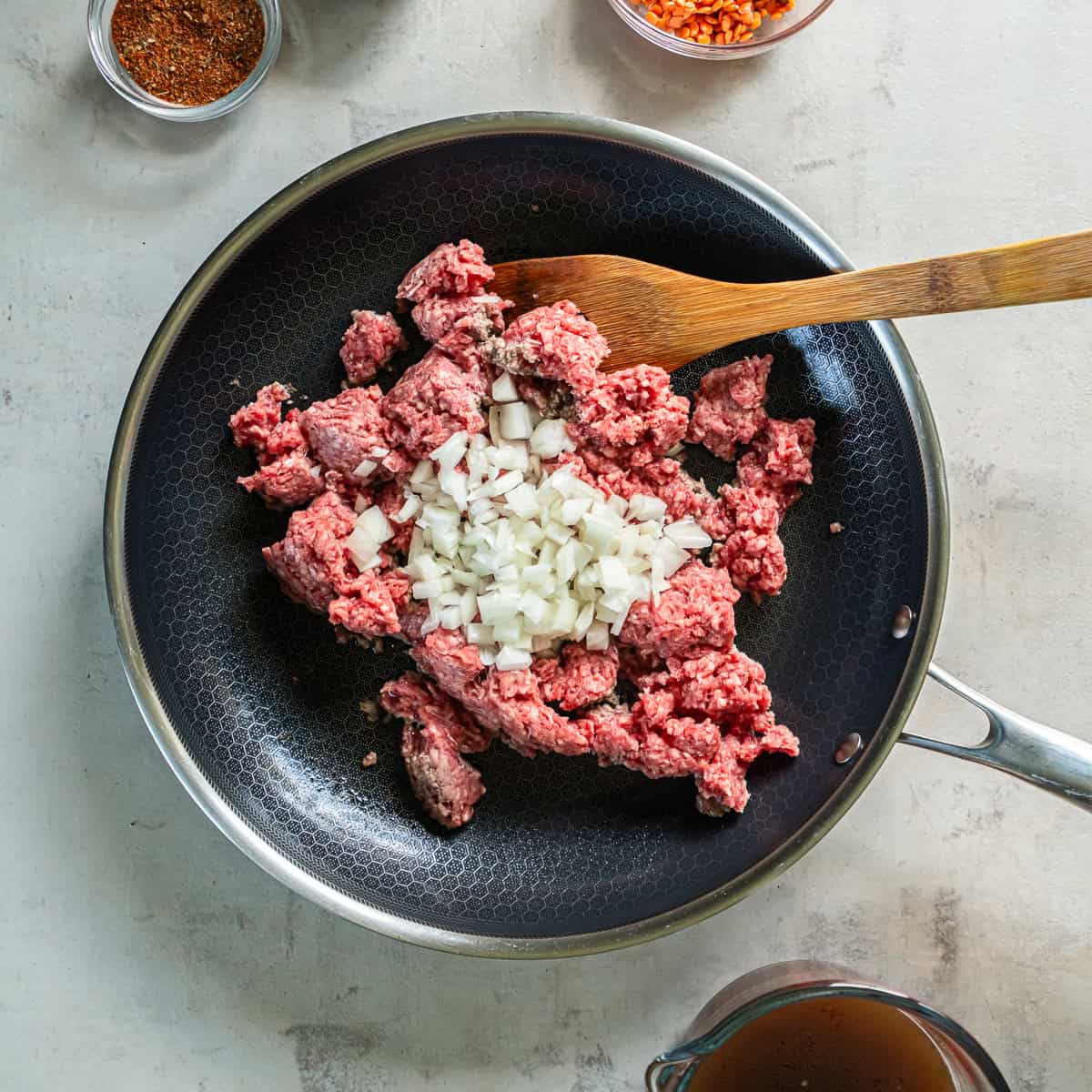 Ground beef and diced onion cooking together in a nonstick skillet.