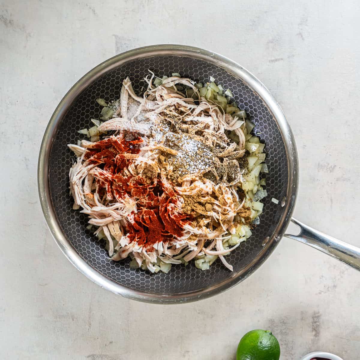 Shredded rotisserie chicken and taco seasonings added to sautéed onion in a skillet.