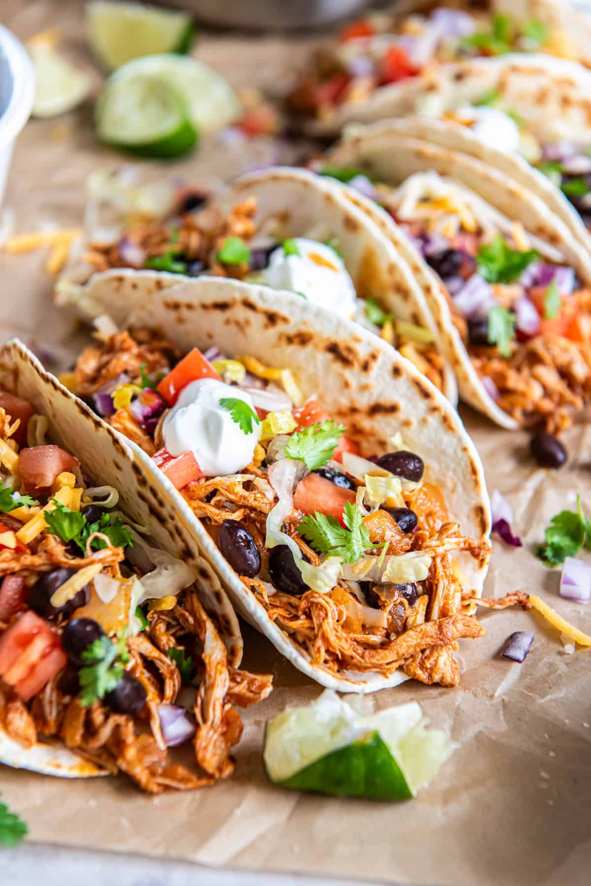 Rotisserie Chicken Tacos with black beans, tomatoes, lettuce, cheese, red onion, cilantro, and sour cream.
