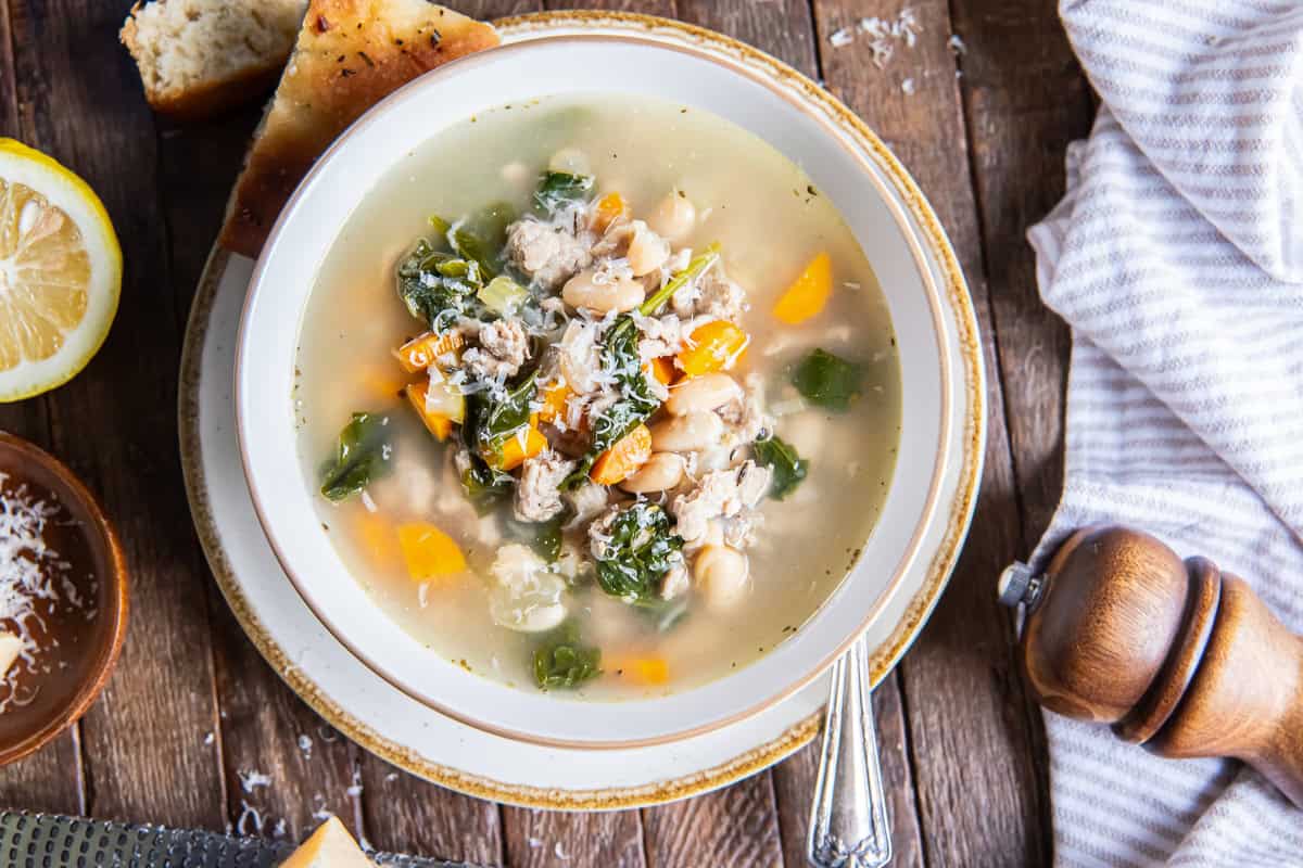 Turkey White Bean Soup with ground turkey, cannellini beans, spinach, carrots, and Parmesan, surrounded by crusty bread, a second bowl of soup, and a wedge of Parmesan.