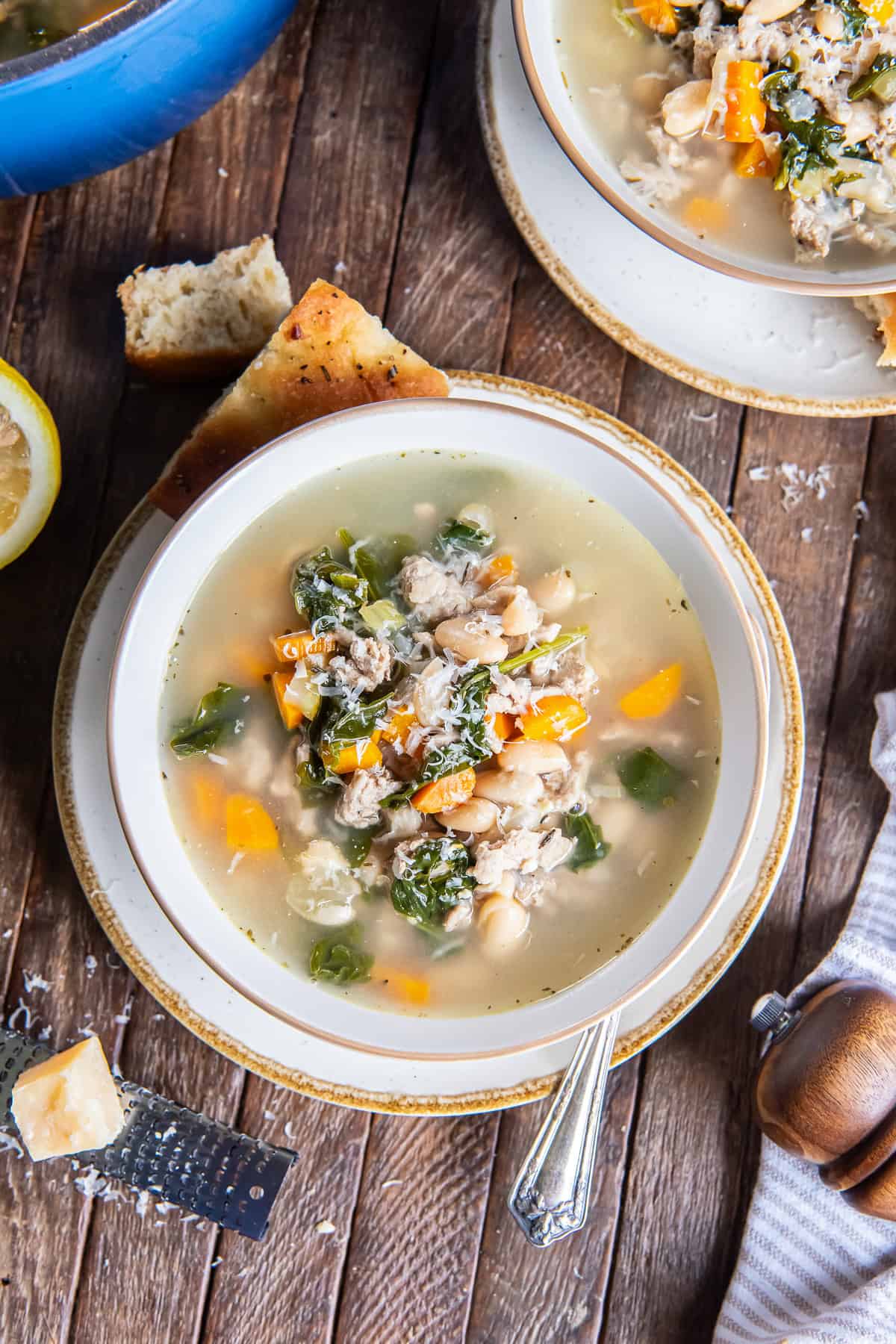 Turkey White Bean Soup with ground turkey, cannellini beans, spinach, carrots, and Parmesan, surrounded by crusty bread, a second bowl of soup, and a wedge of Parmesan.