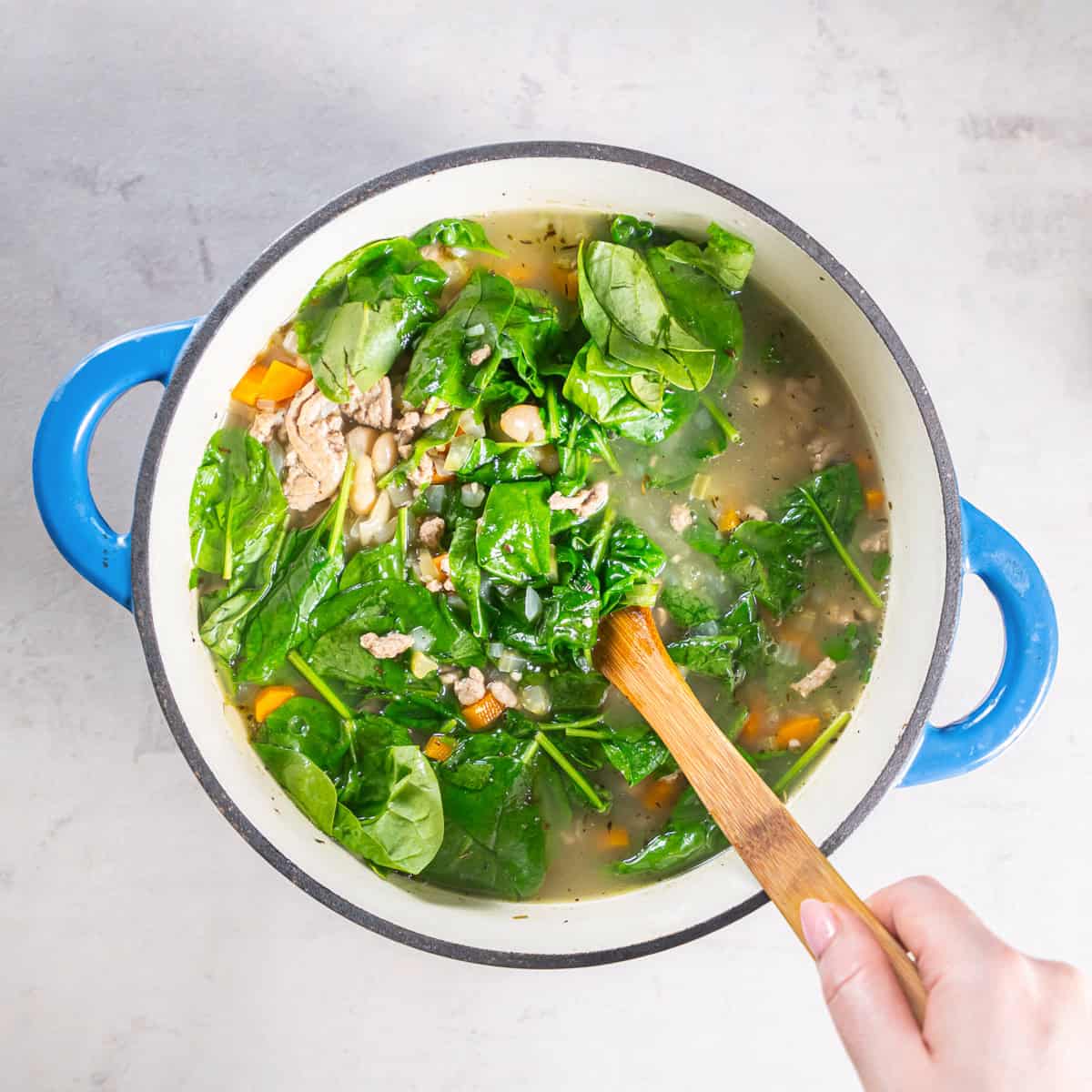 Fresh baby spinach being stirred into the turkey white bean soup.