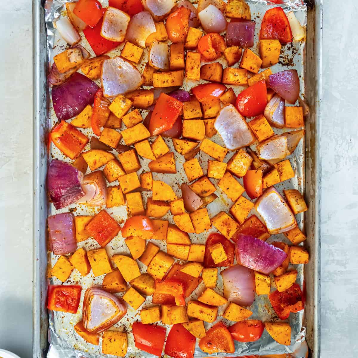 Seasoned cubes of sweet potato, red bell pepper and onion on a baking sheet.